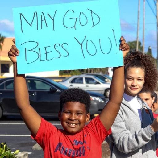A boy holding a handwritten sign reading May God bless you at a See His Face Ministries outreach